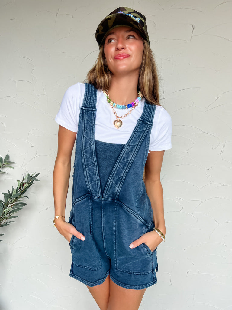 Woman wearing denim overalls and a white t-shirt against a white wall.