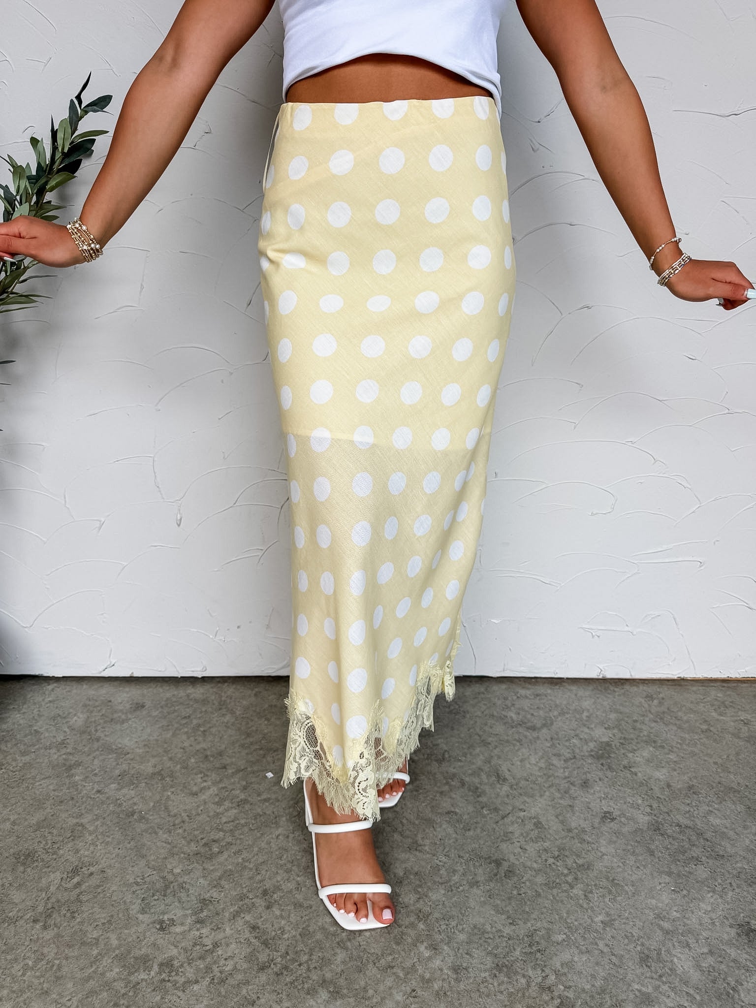 Person wearing a yellow polka dot skirt with a white top against a plain background