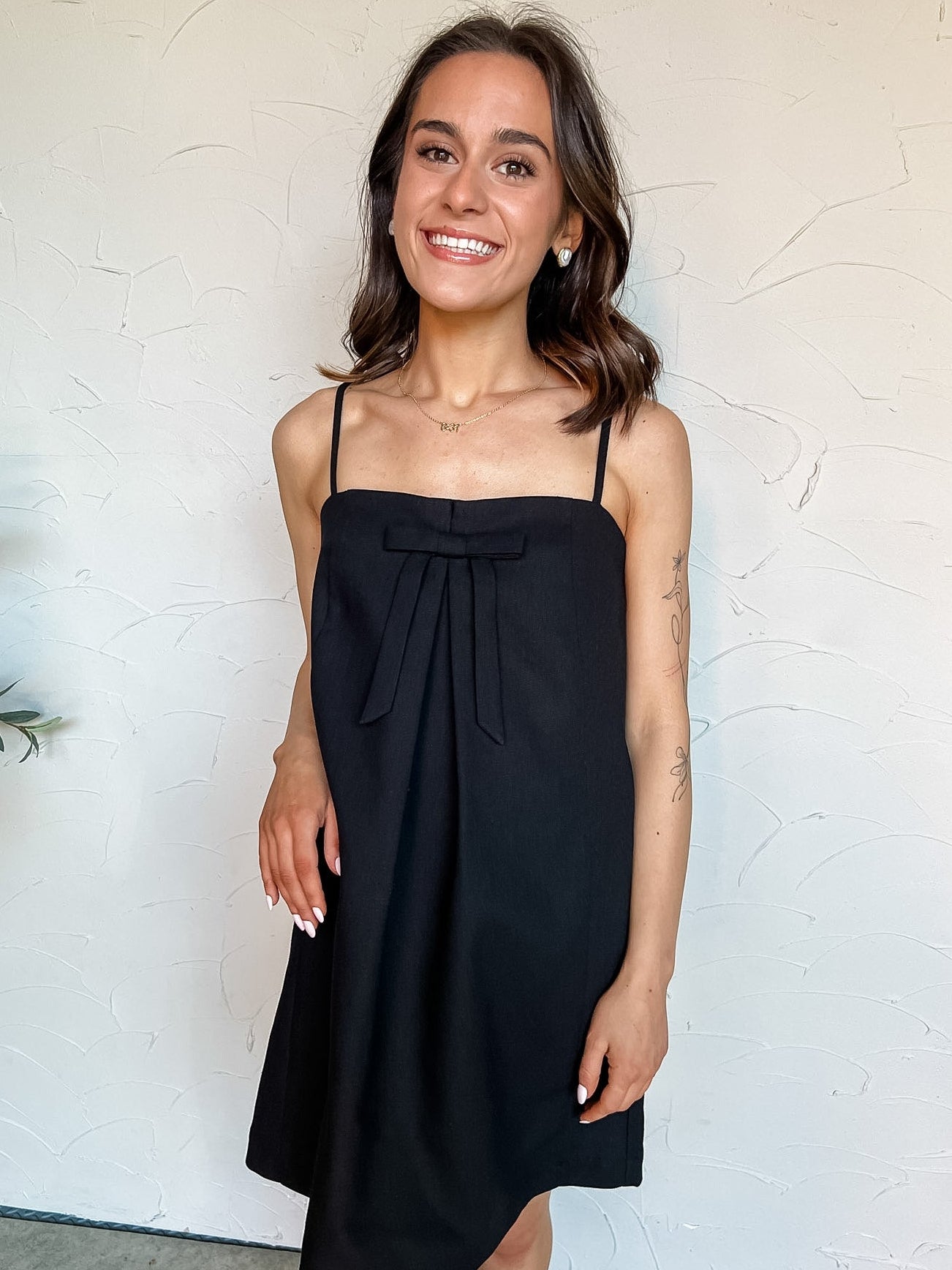 Woman wearing a black dress with a bow against a white wall