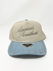 A cream hat that says "America's Sweetheart" with silver script and stitched stars with a denim blue bill.