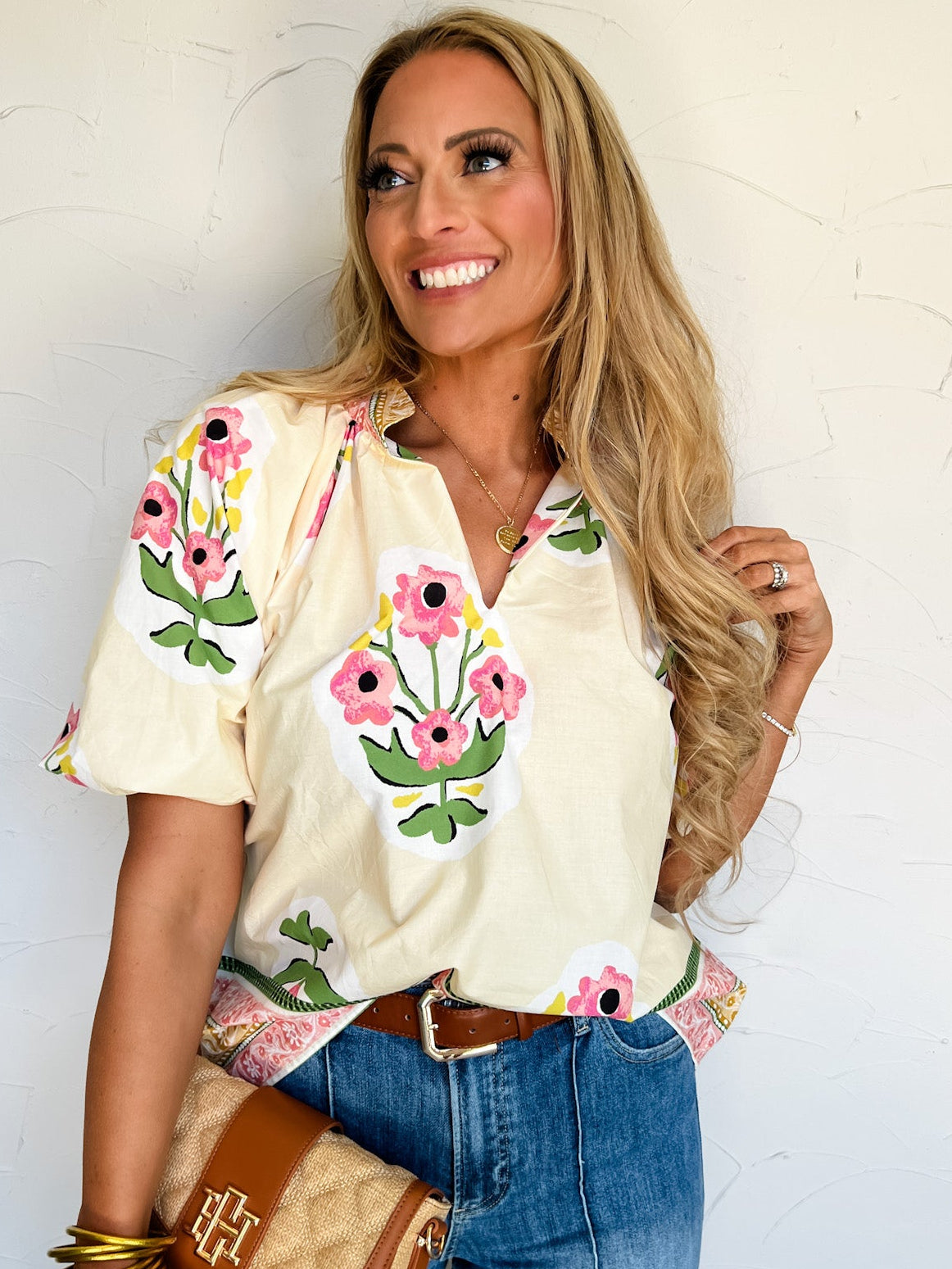 Woman wearing a floral embroidered and holding a handbag against a white wall