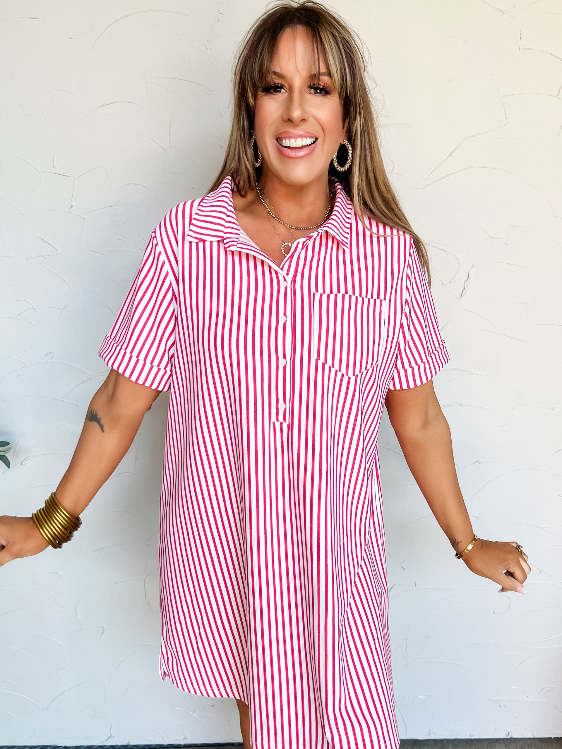 Woman wearing a hot pink and white striped t-shirt dress against a plain background
