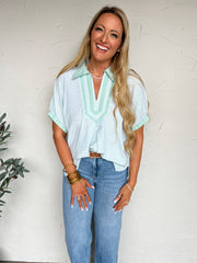 Woman wearing a light blue striped shirt and jeans against a white wall.