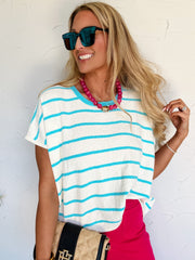 Woman wearing a striped shirt and sunglasses against a white wall