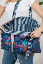 Person holding a navy blue bag with colorful bird pattern and striped handle.