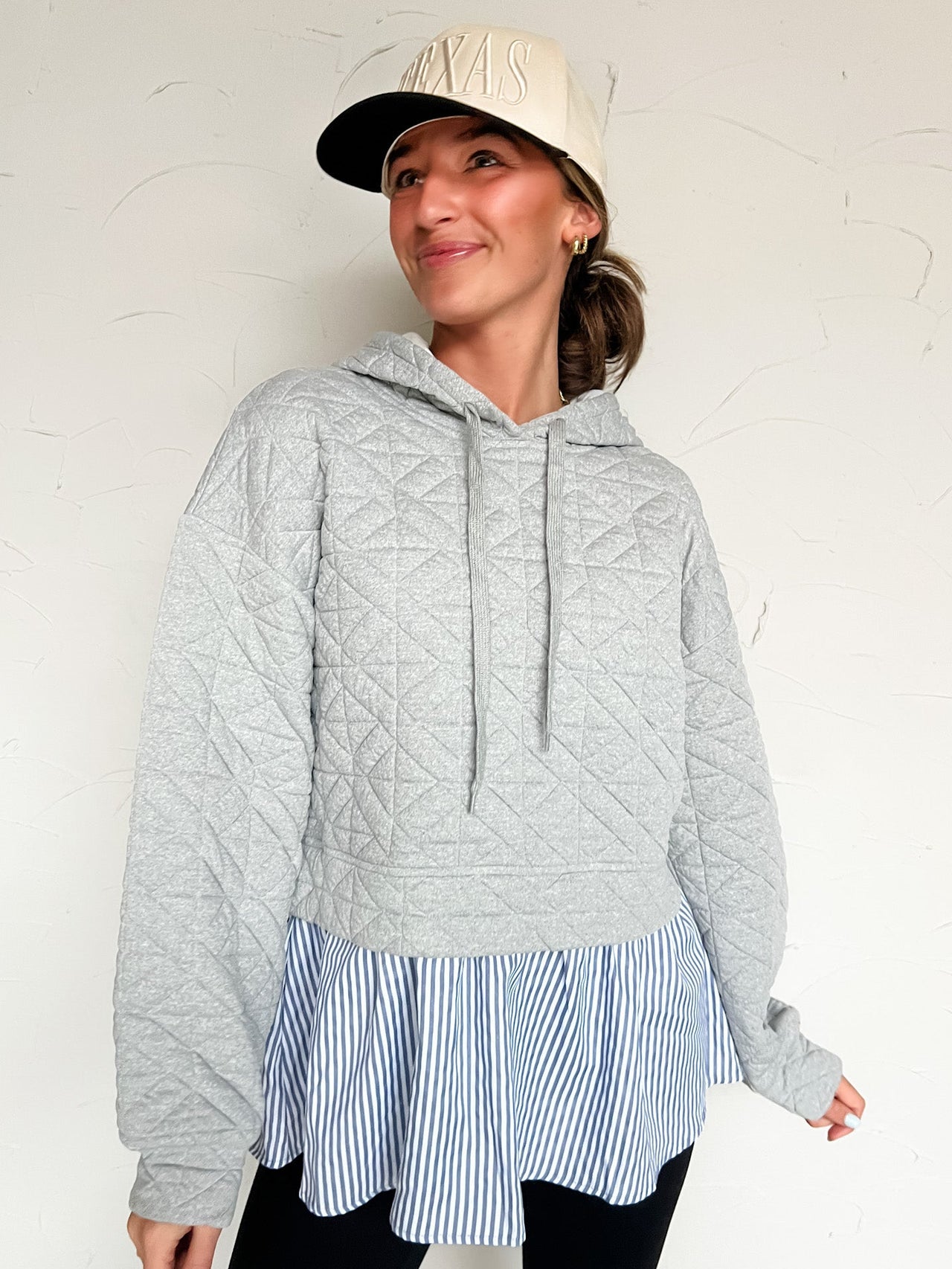 Woman wearing a gray quilted hoodie with a striped shirt built in coming out bottom with a white background
