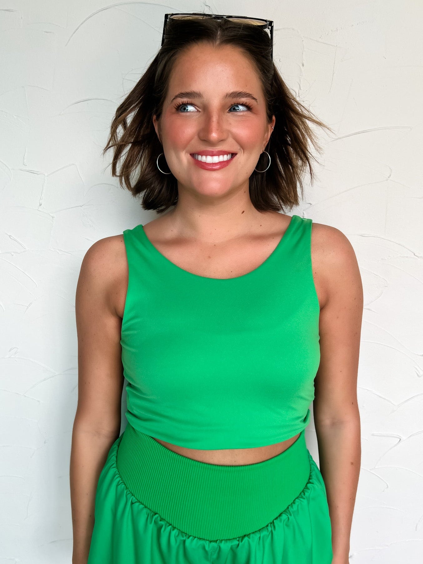 Woman wearing a green tank top and shorts outfit against a white wall