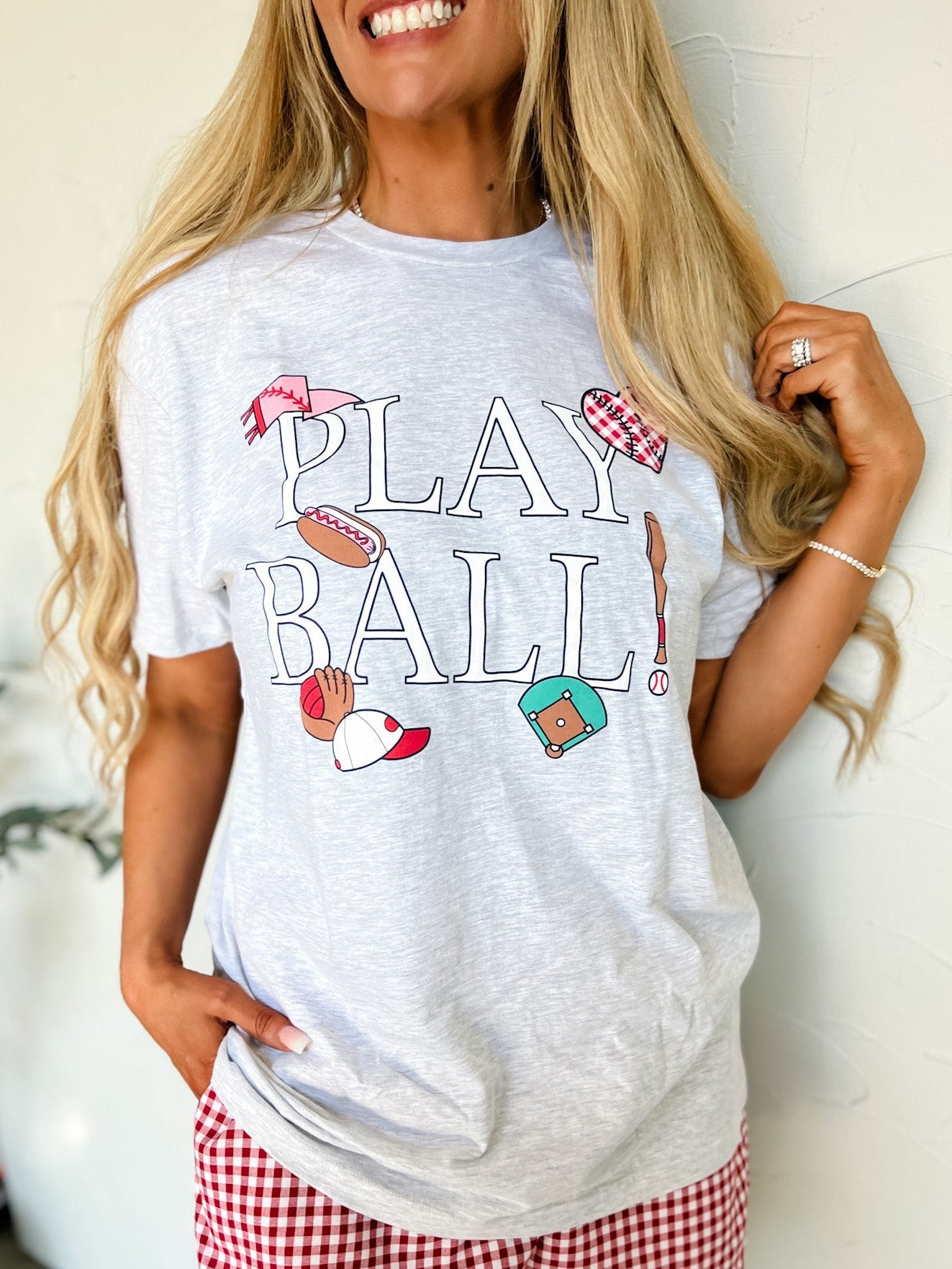 Woman wearing a 'Play Ball' t-shirt with graphics and red checkered shorts.