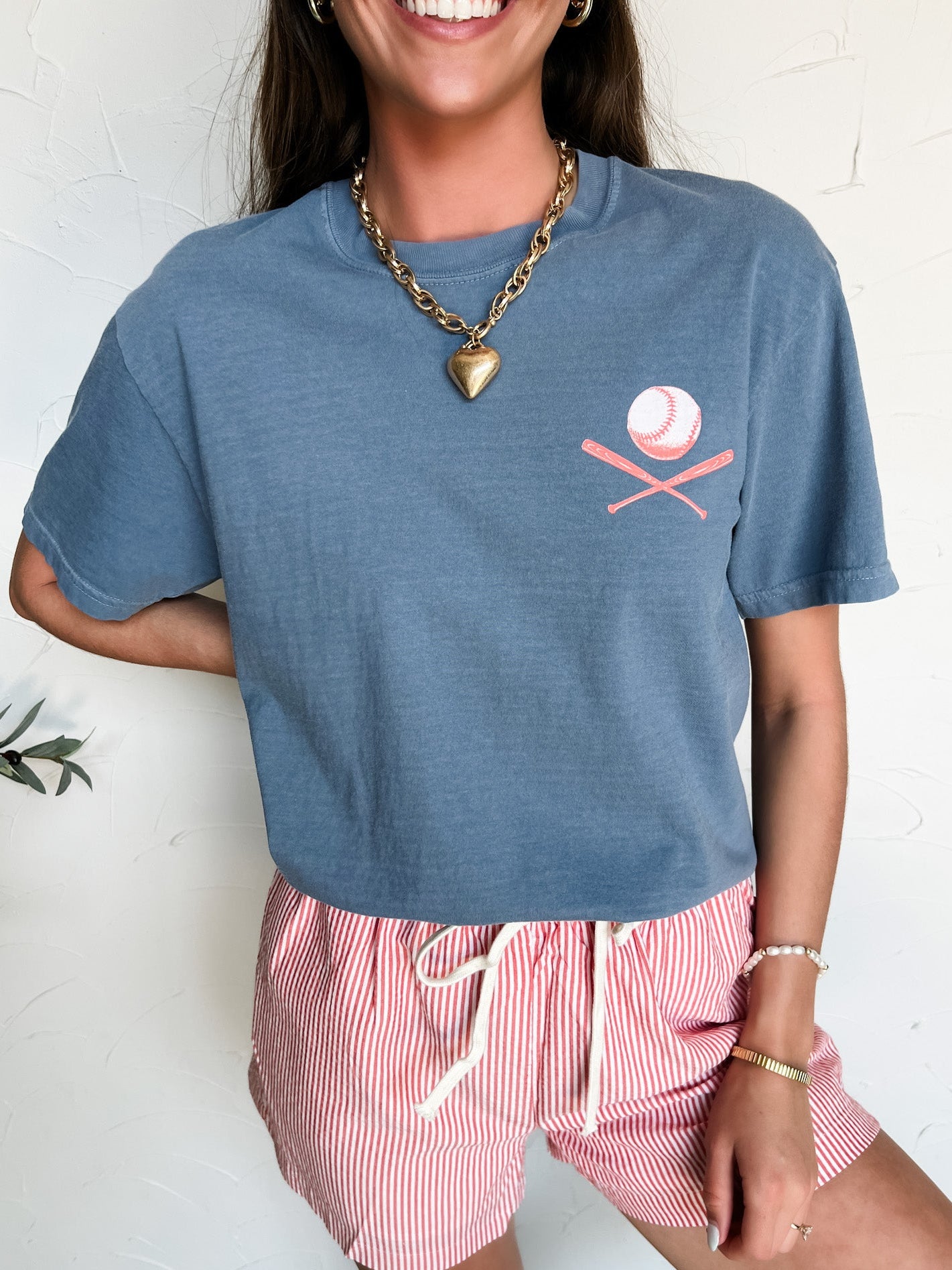 Person wearing a blue t-shirt with a pink baseball logo and red striped shorts on a white background