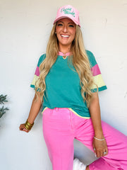 Woman wearing a teal and pink outfit with a cap against a white wall