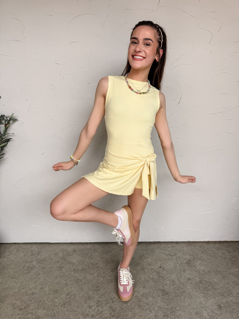 Young girl in a yellow dress posing against a plain wall.