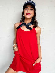 Woman wearing a red athletic dress with built in shorts and navy cap with a white background