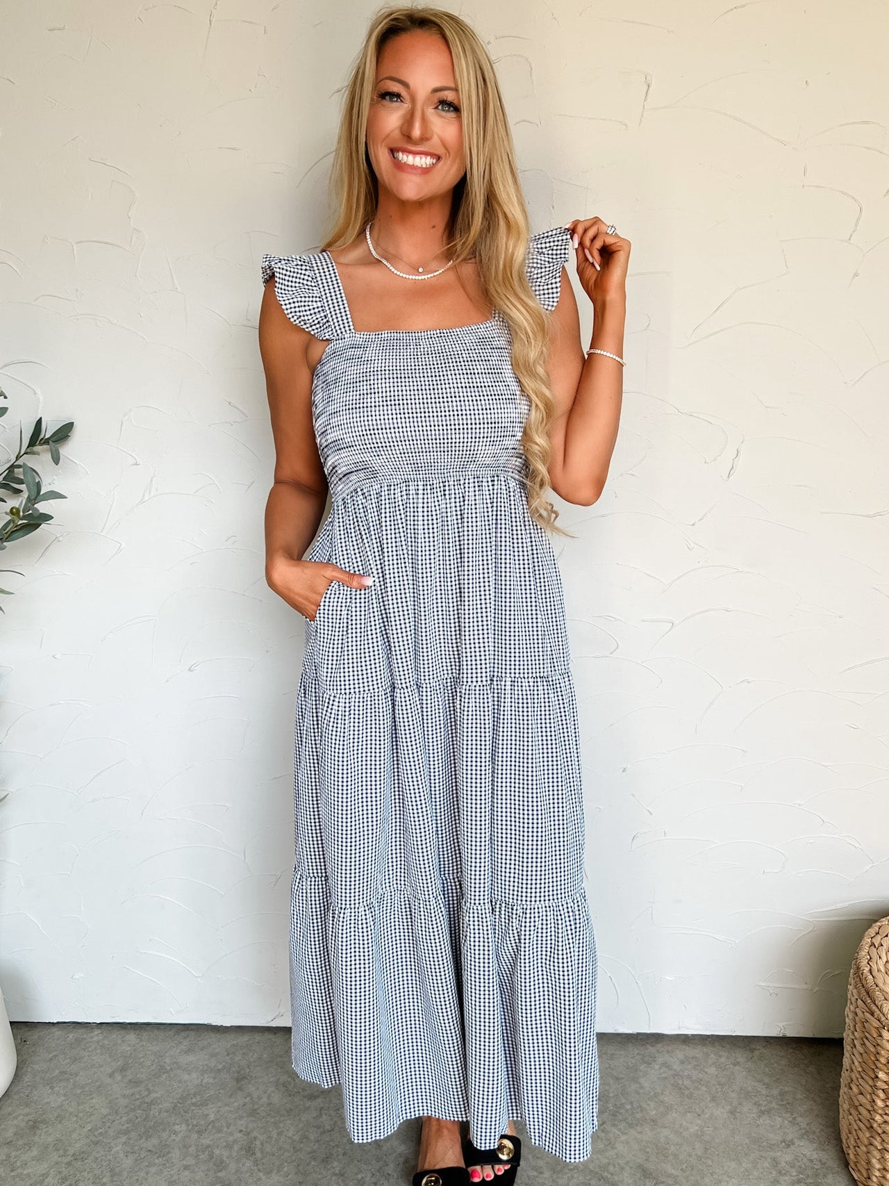 Woman wearing a blue checkered dress standing against a white wall.