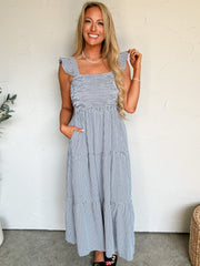 Woman wearing a blue checkered dress standing against a white wall.