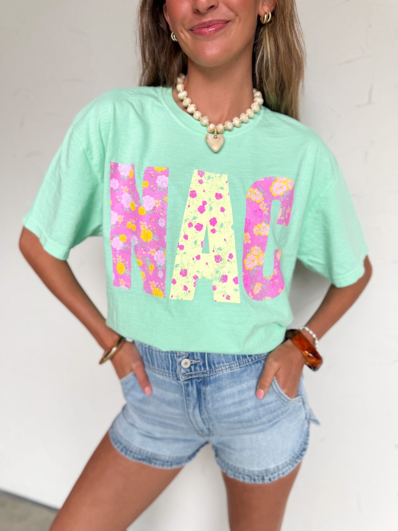 mint green graphic t-shirt with N-A-C spelled out in bright floral print in pinks and yellows.