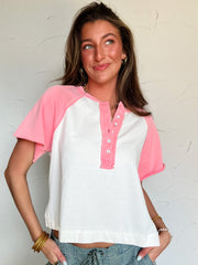 Woman wearing a white and pink baseball-style shirt against a plain background