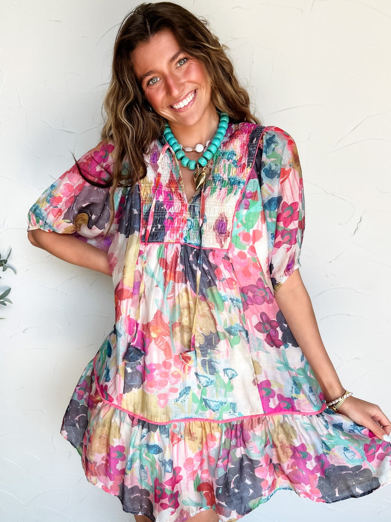 Woman wearing a colorful watercolor floral short dress against a white wall