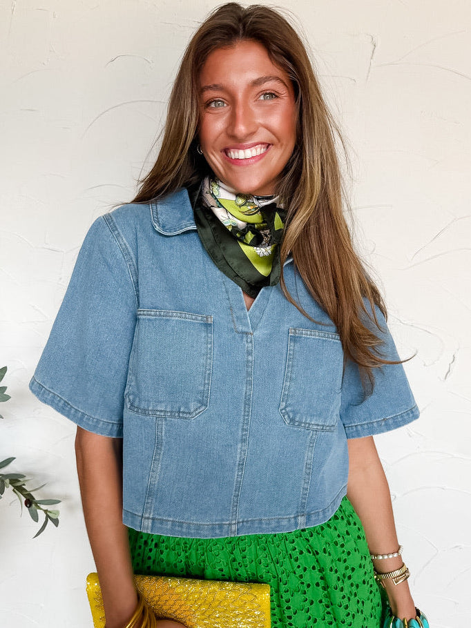 Woman wearing a blue denim shirt, green skirt, and yellow clutch against a white background