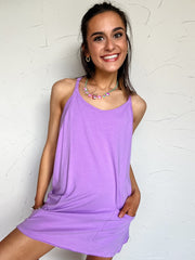 Woman wearing a purple dress posing against a white wall