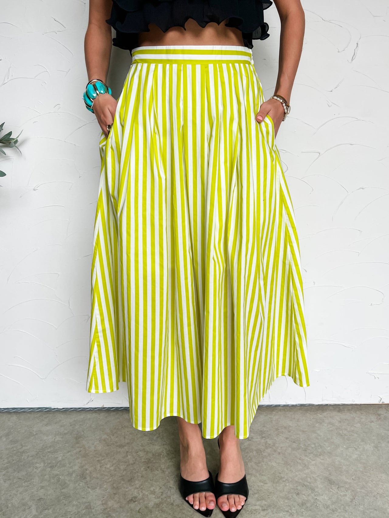 Person wearing a light green and white striped skirt against a white wall.