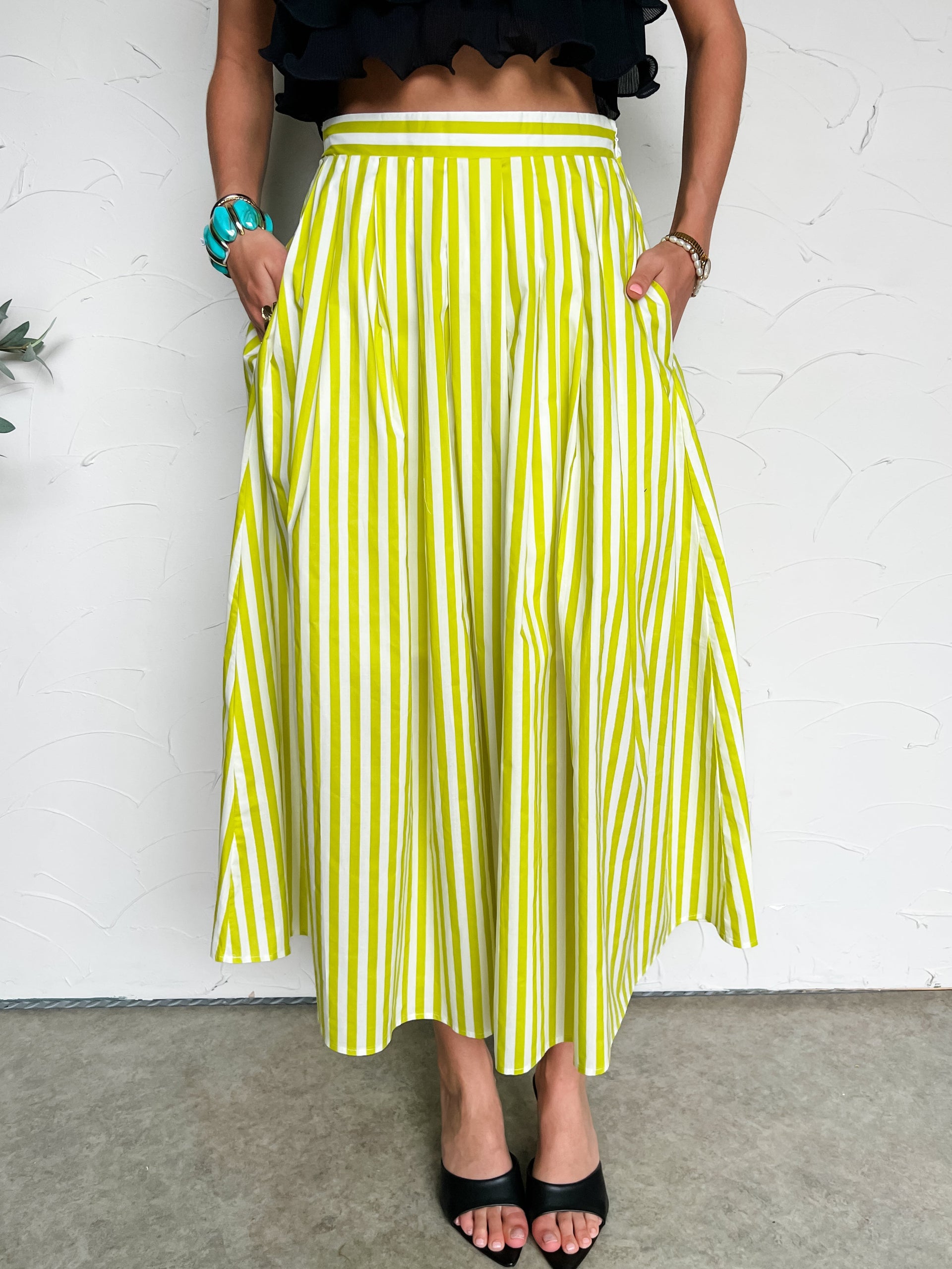 Person wearing a light green and white striped skirt against a white wall.