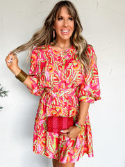 Woman wearing a colorful patterned dress against a white wall.
