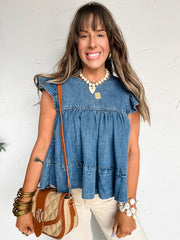 Woman wearing a blue top with ruffled sleeves, holding a brown purse against a white background