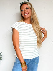 Woman wearing a green and white striped shirt and blue jeans against a white wall.