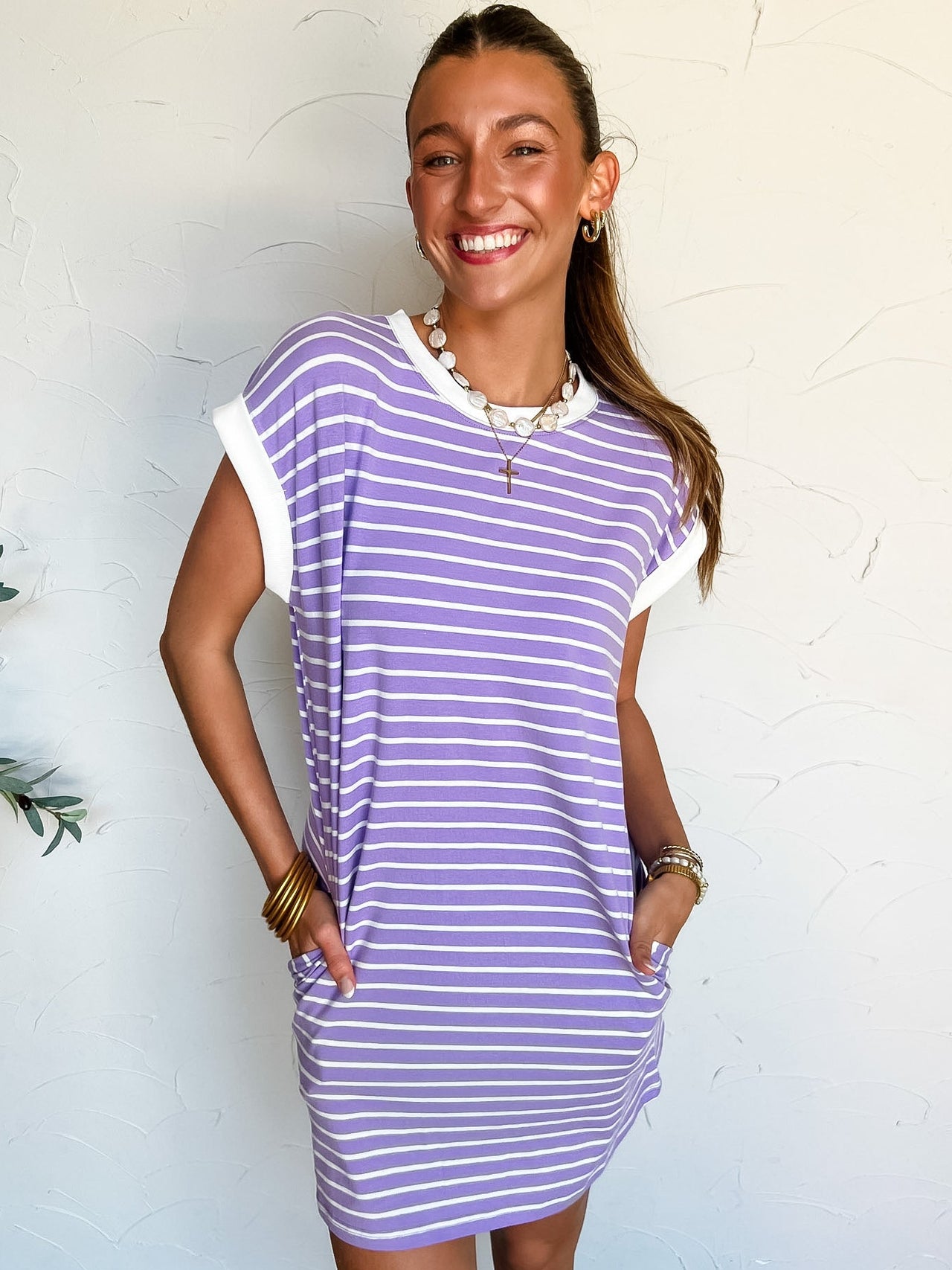 Woman wearing a purple and white striped t-shirt dress against a white wall.