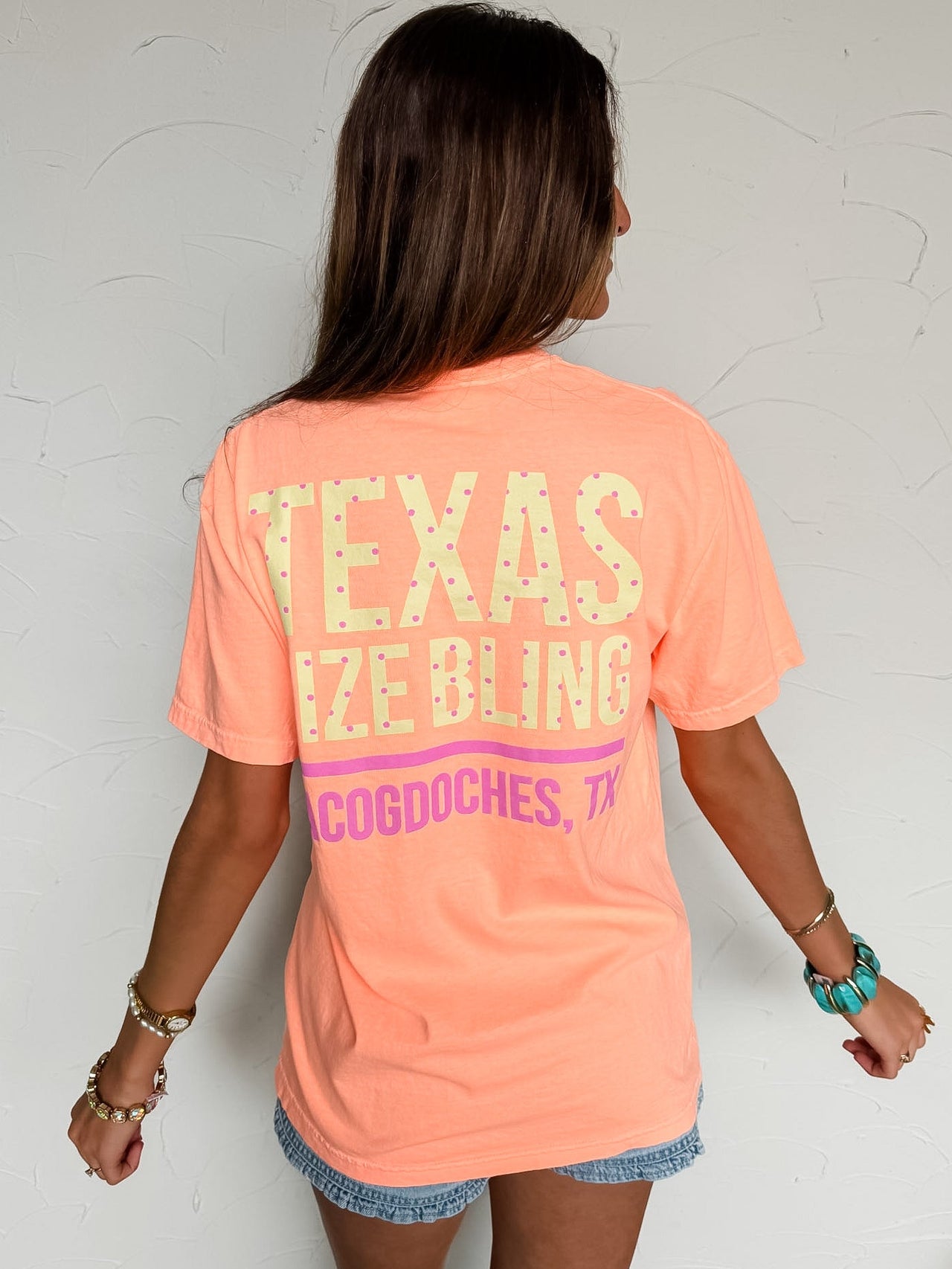 Person wearing a peach t-shirt with 'TSB' text against a white wall