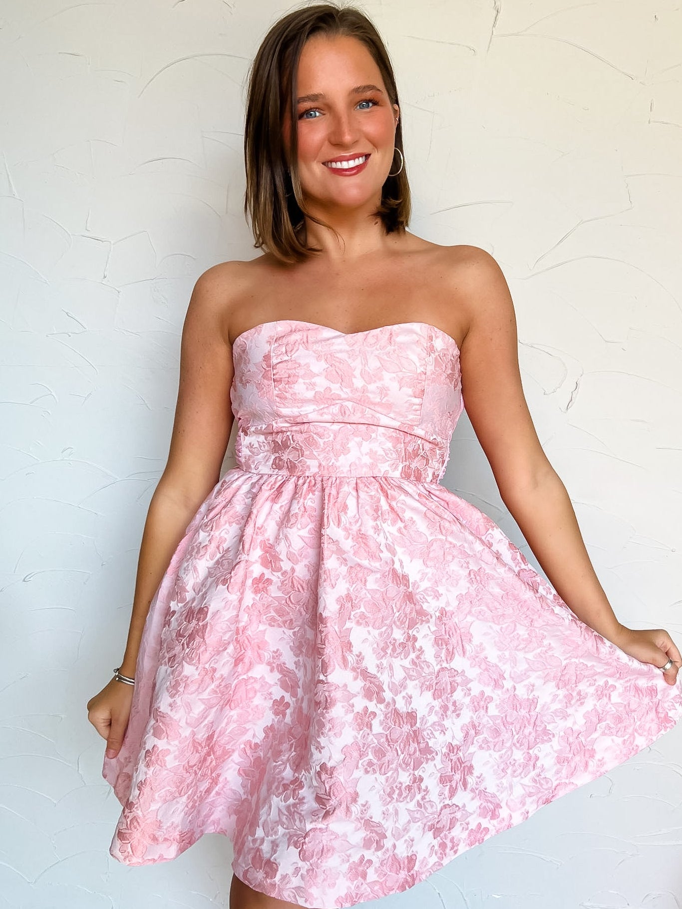 Woman wearing a pink floral strapless dress against a white background