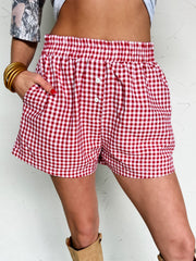Person wearing red and white checkered shorts with beige knee-high boots against a white background