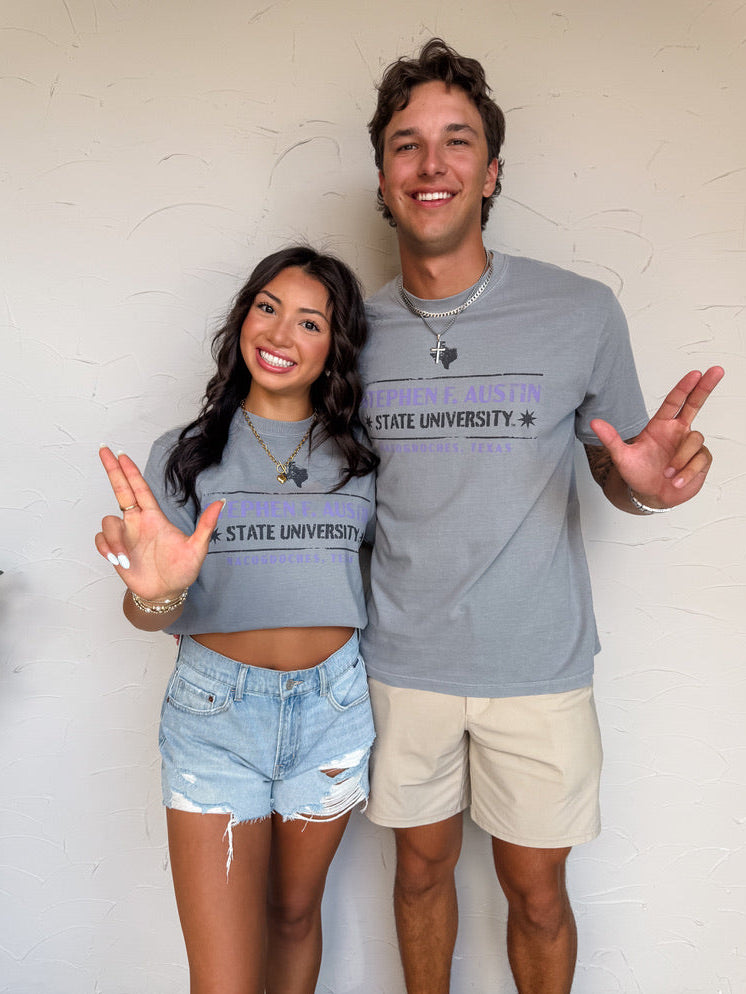 Two people wearing matching gray 'Stephen F Austin' shirts against a white wall.