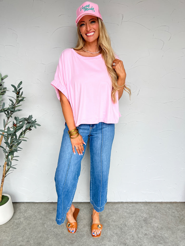 Woman wearing a pink top and jeans with a pink cap indoors.