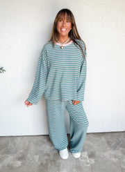 Lesly modeling the Anniewear In My Element Brushed Stripe Pants Set in size Large, made from 92% polyester and 8% spandex, featuring green horizontal stripes with light and dark accents, a round-neck long-sleeve top with dropped shoulders, and matching full-length wide-leg pants with a gathered drawstring waist.