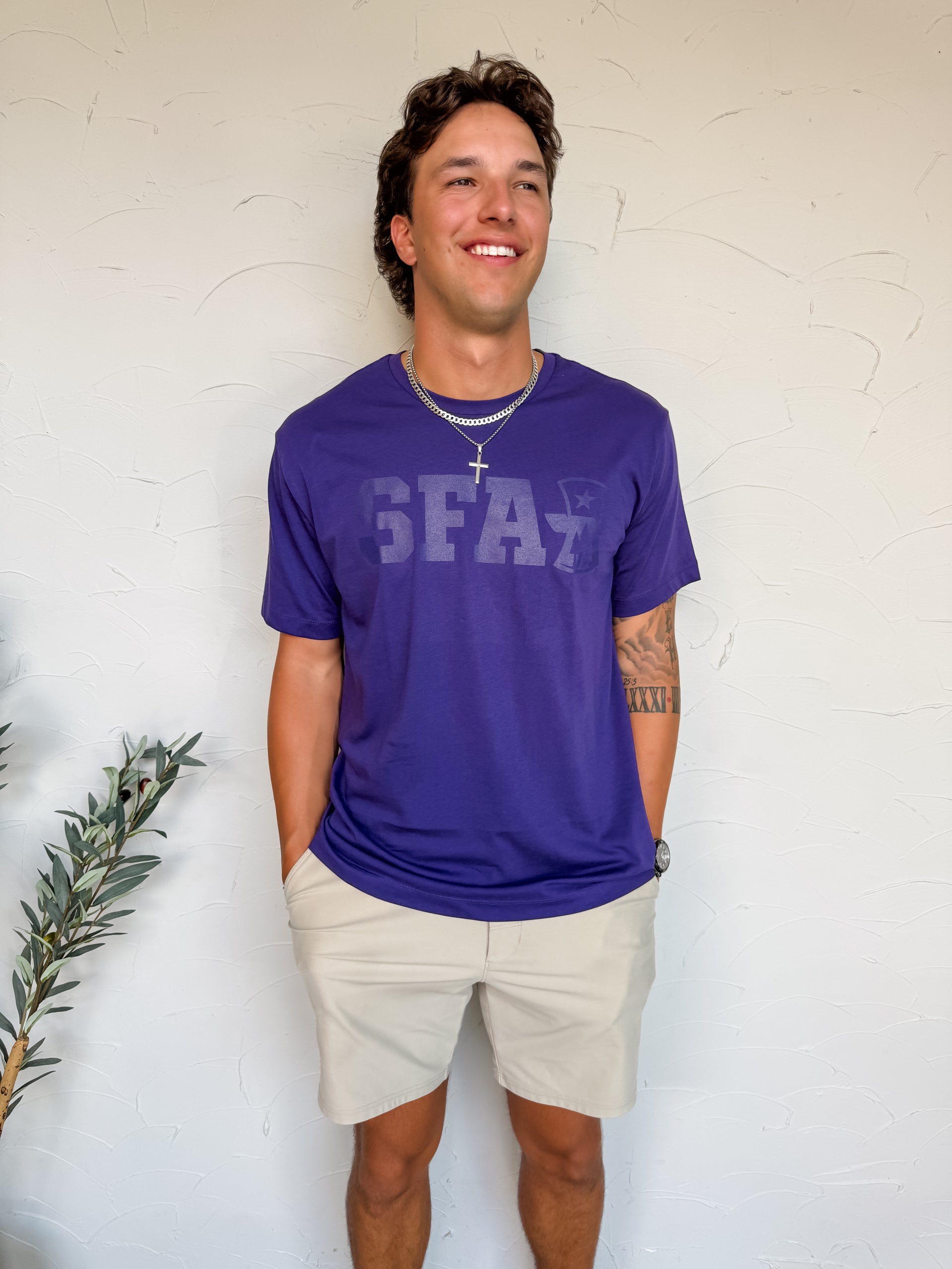 Man wearing a purple t-shirt with 'SFA' text, standing against a white wall.
