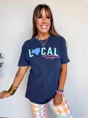 Woman wearing a navy blue t-shirt with colorful text and graphics, standing against a white wall.