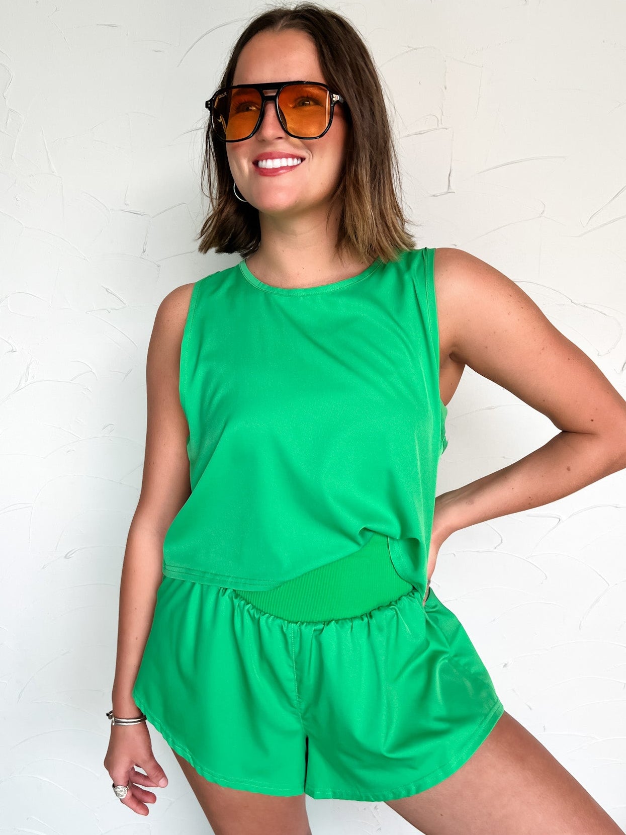 Woman wearing a green outfit with sunglasses against a white background