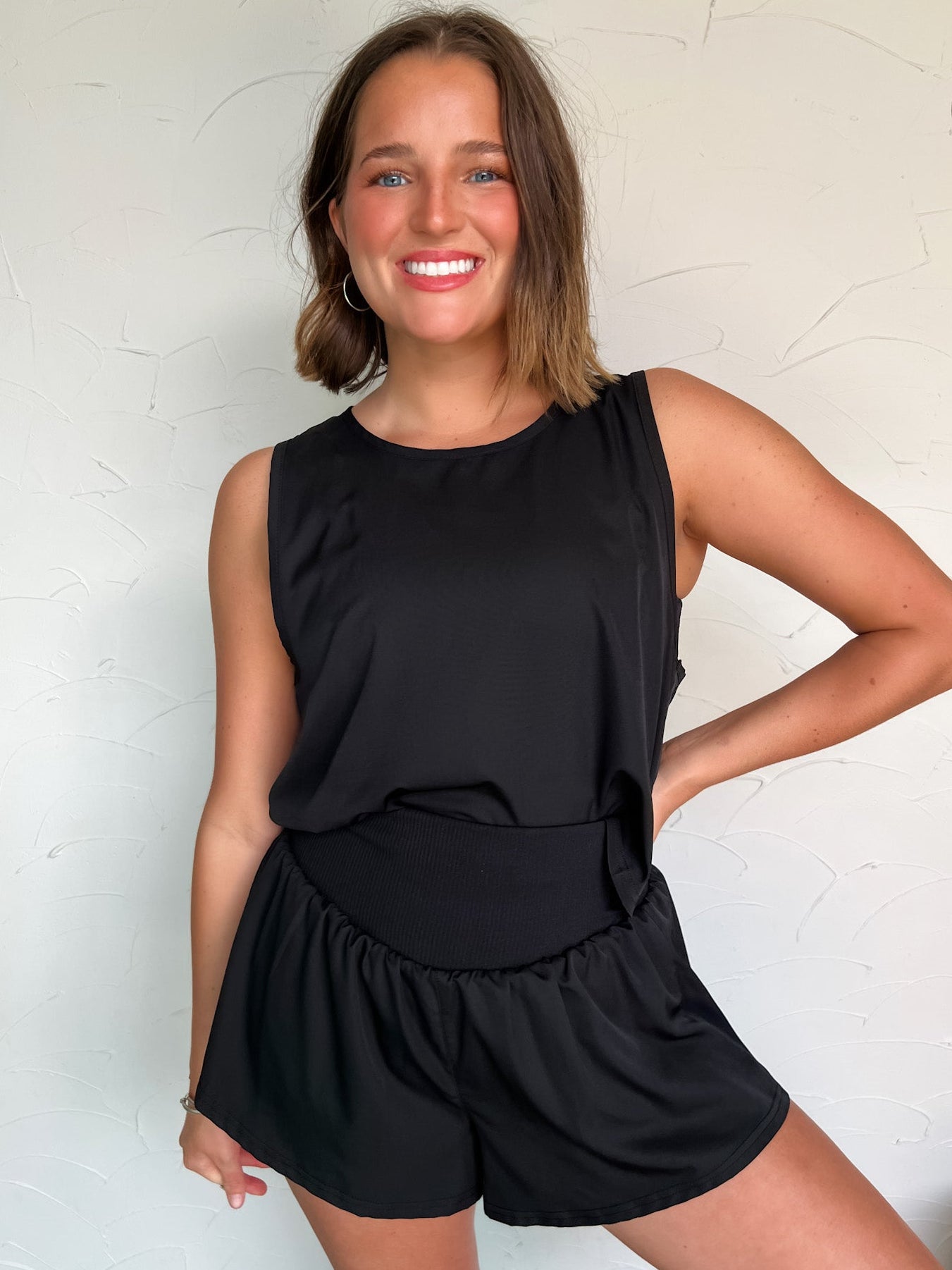Woman wearing a black sleeveless top and shorts against a white wall
