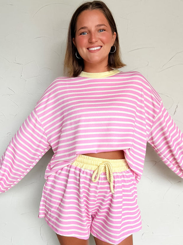 Woman wearing a pink and white striped set with a yellow waistband against a white background