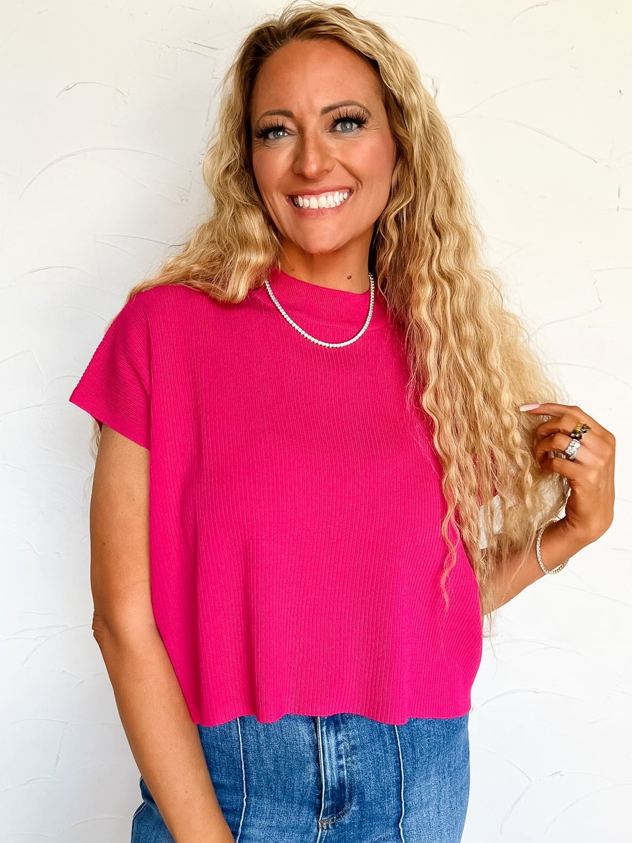 Woman wearing a bright pink sweater top and blue jeans against a white background