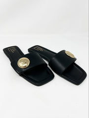 Pair of single strap black sandals with gold round detail on strap on a white background