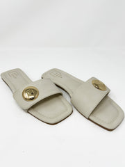 Pair of single strap beige sandals with gold round detail on strap on a white background