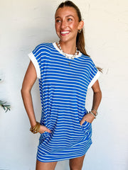 Woman wearing a blue and white striped t-shirt dress against a white wall.