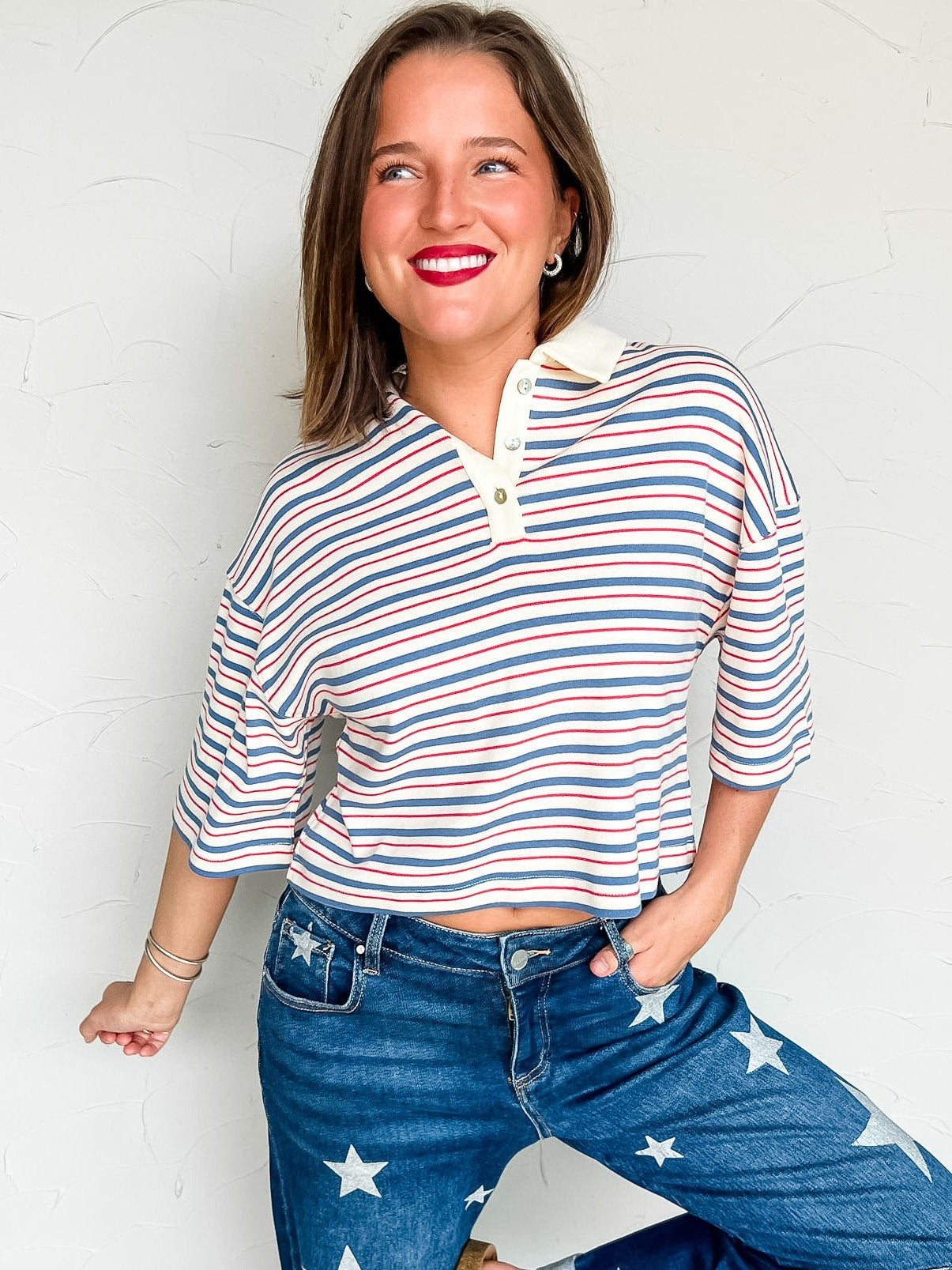 Woman wearing a blue red & white striped shirt and star-patterned jeans against a white brick wall.