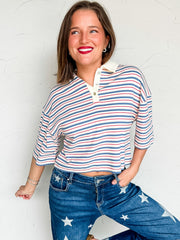 Woman wearing a blue red & white striped shirt and star-patterned jeans against a white brick wall.