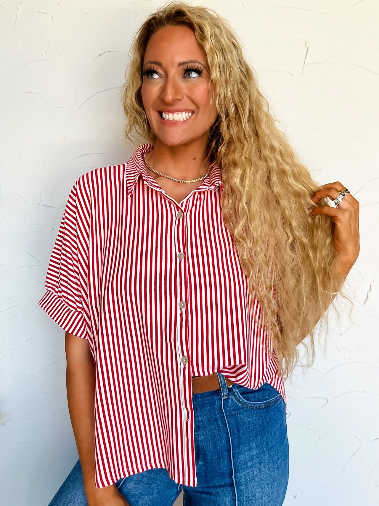 Woman wearing a red and white striped button up shirt and blue jeans against a light background