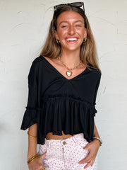 Woman wearing a black top and Pink polka dot pants against a white wall