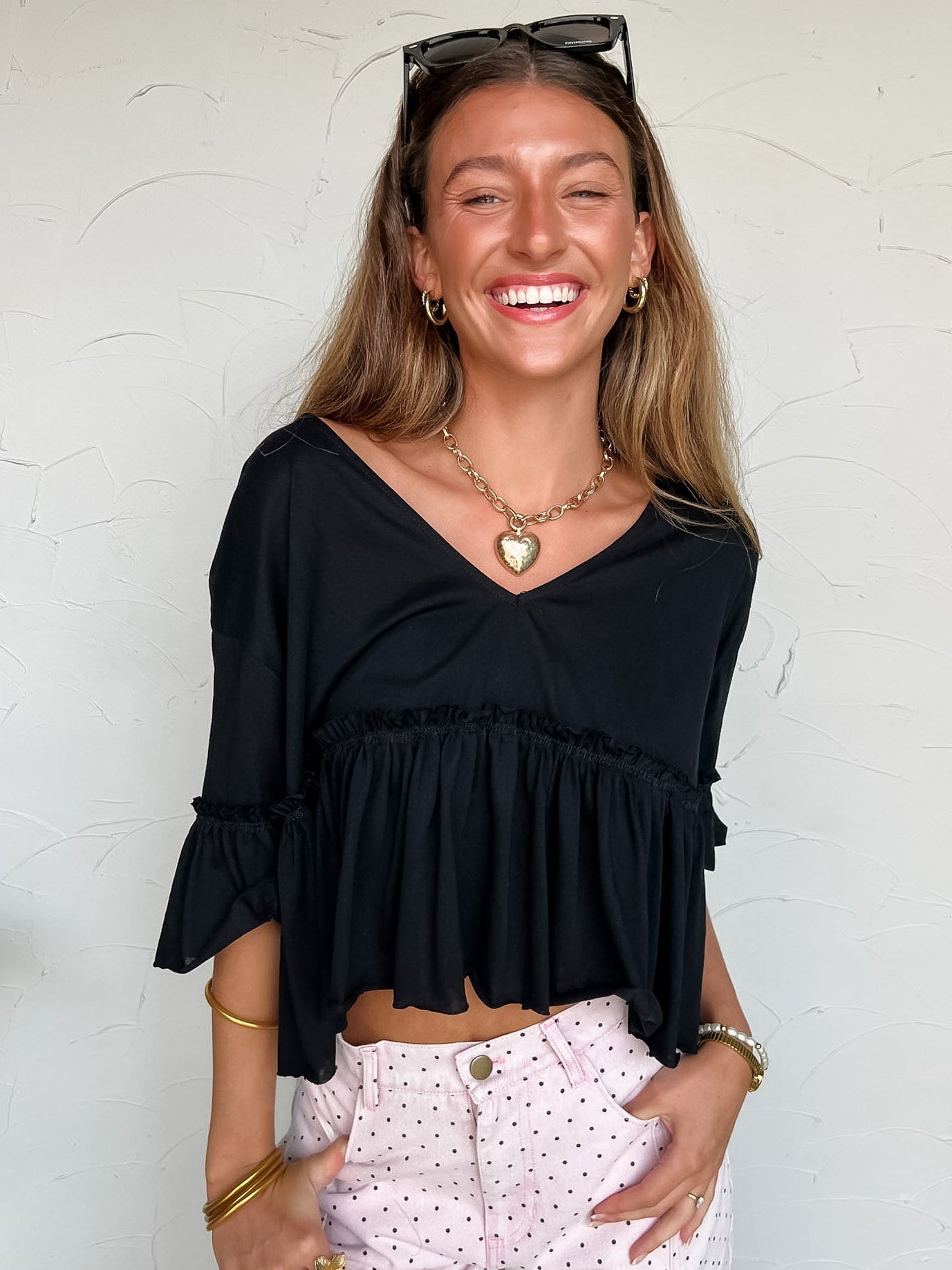 Woman wearing a black top and Pink polka dot pants against a white wall