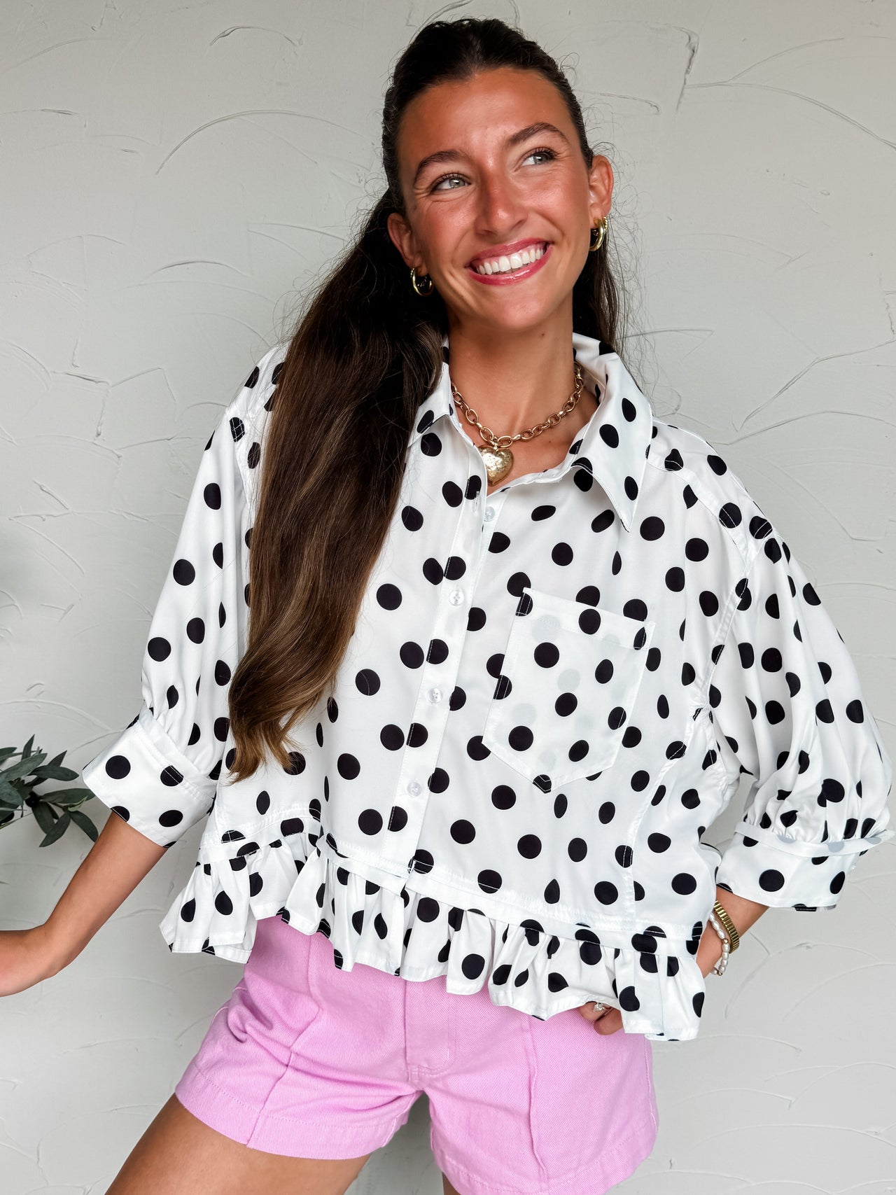 Woman wearing a white blouse with black polka dots and pink shorts against a light background